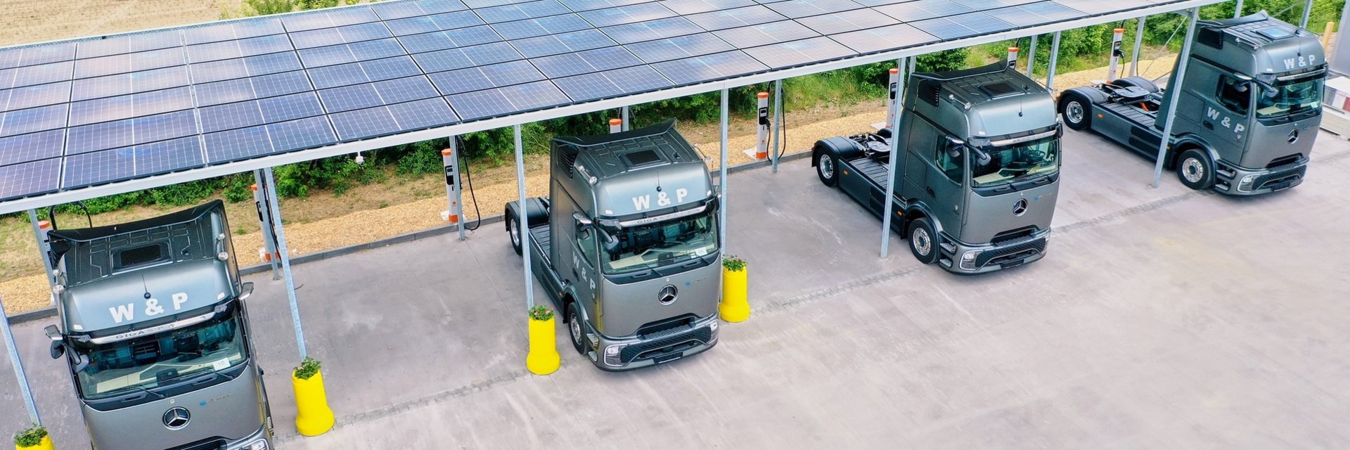 W&P electric trucks connected to chargers beneath a line of solar panels
